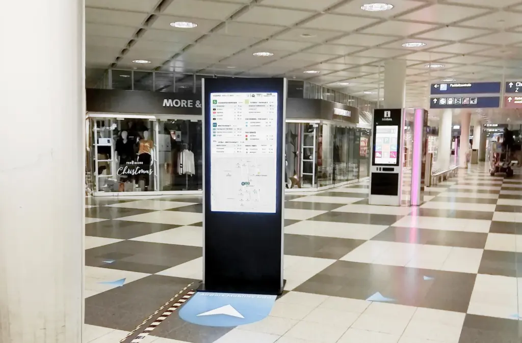 Der VEOMO-Mobilitätsmonitor im Einsatz – Am Flughafen. Der Bildschirm zeigt Abfahrtszeiten von ÖPNV, Sharing-Angebote und eine Umgebungskarte.