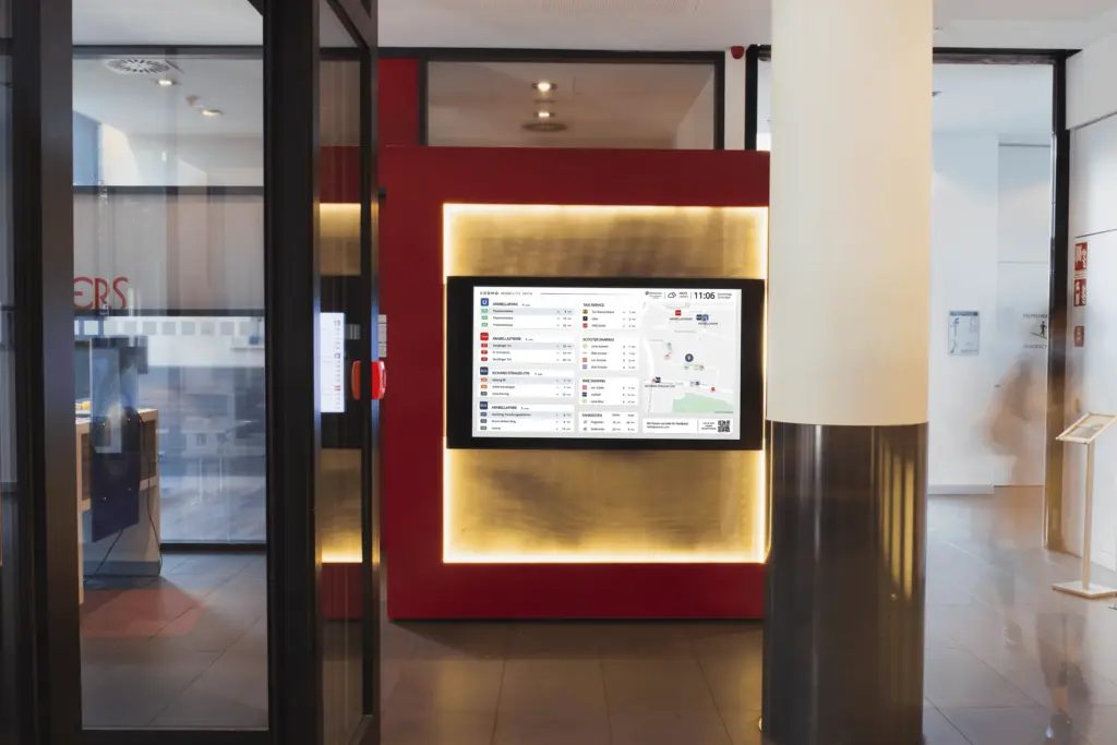 Der VEOMO-Mobilitätsmonitor im Einsatz – Für die Hotellobby. Der Bildschirm zeigt Abfahrtszeiten von ÖPNV, Sharing-Angebote und eine Umgebungskarte.