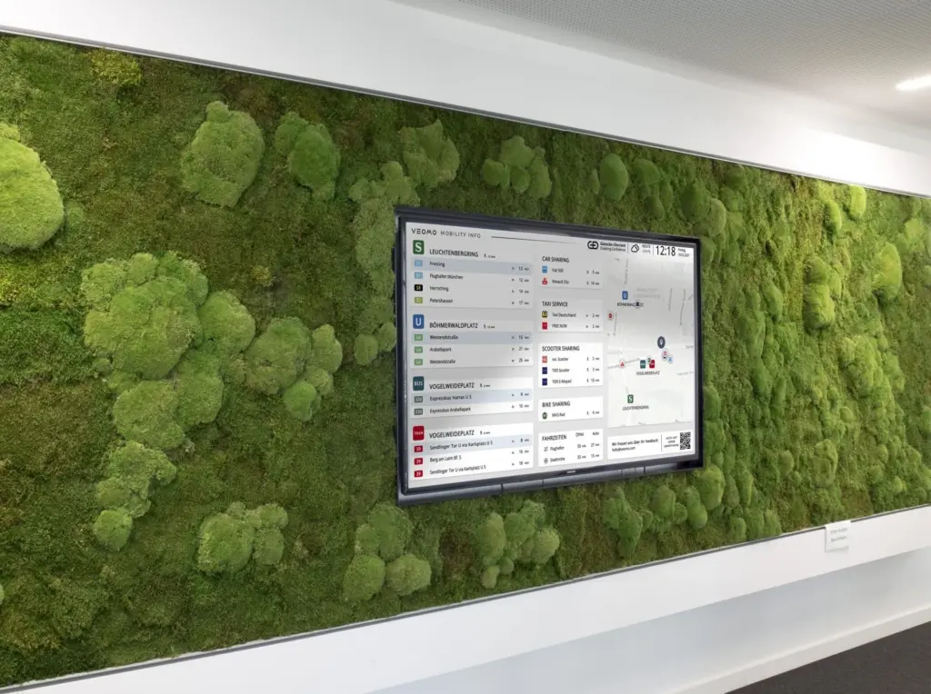Der VEOMO-Mobilitätsmonitor im Einsatz – Im Office. Der Bildschirm zeigt Abfahrtszeiten von ÖPNV, Sharing-Angebote und eine Umgebungskarte.