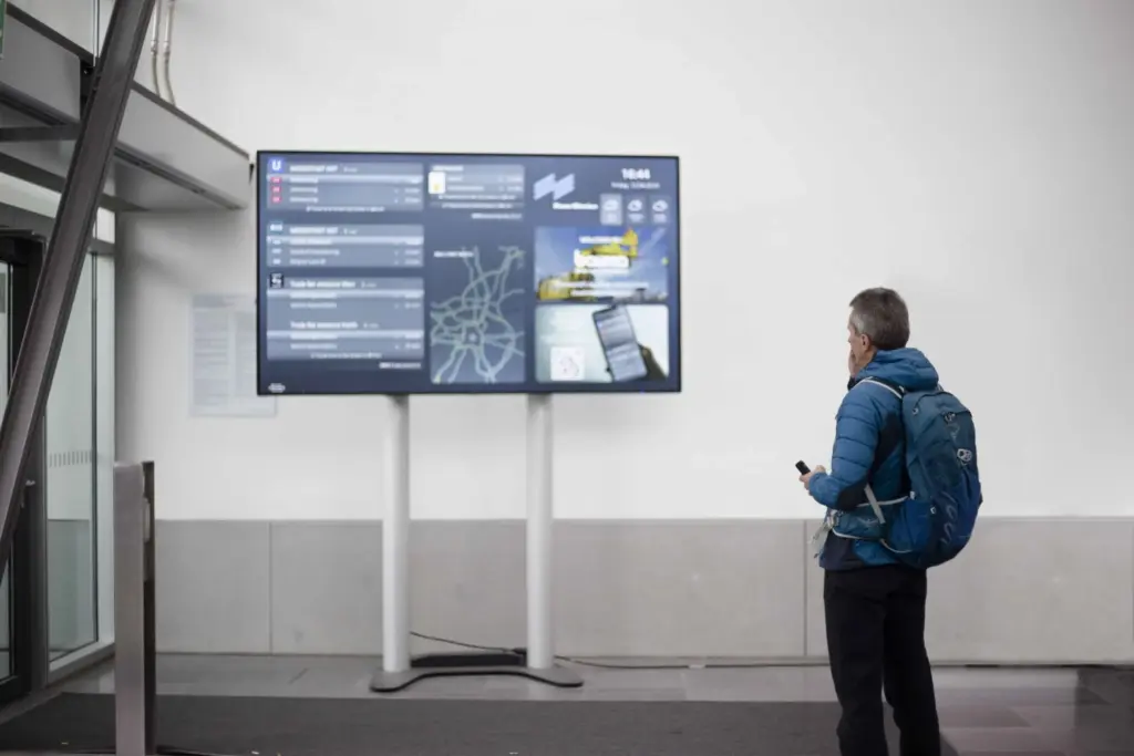 Der VEOMO-Mobilitätsmonitor im Einsatz – In der Messe. Der Bildschirm zeigt Abfahrtszeiten von ÖPNV, Sharing-Angebote und eine Umgebungskarte.