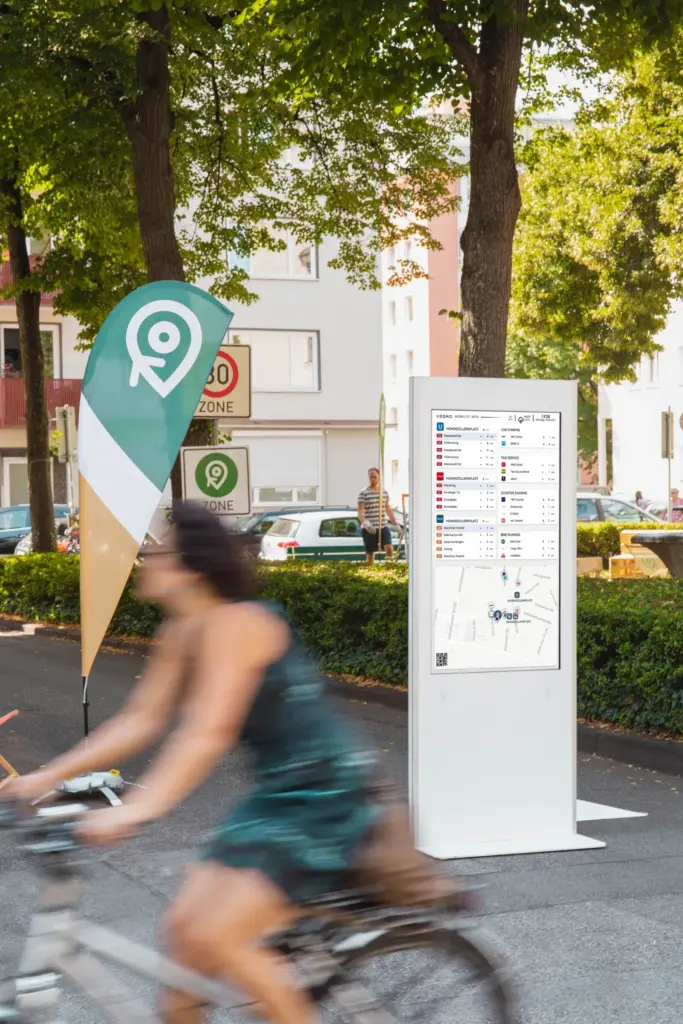 Der VEOMO-Mobilitätsmonitor im Einsatz – Auf öffentlichen Plätzen. Der Bildschirm zeigt Abfahrtszeiten von ÖPNV, Sharing-Angebote und eine Umgebungskarte.