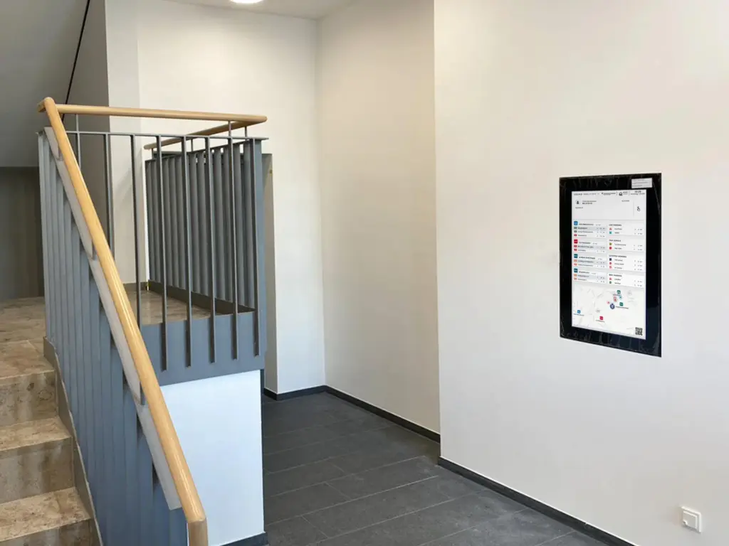 Der VEOMO-Mobilitätsmonitor im Einsatz – In Wohngebäuden. Der Bildschirm zeigt Abfahrtszeiten von ÖPNV, Sharing-Angebote und eine Umgebungskarte.